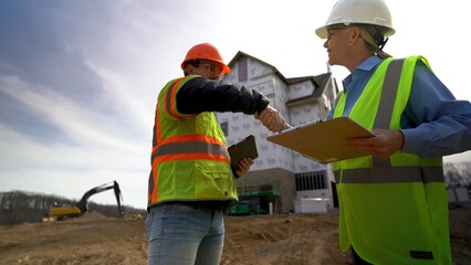 Wide angle view of woman project manager shaking hands with job foreman and walking off the construction site.