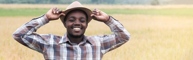African farmer in hat is standing in his growing wheat field.Agriculture or cultivation concept
