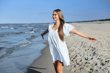 Happy smiling beautiful woman is on the ocean beach in a white summer dress, open arms.