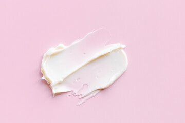 Swatch of white cream texture, cosmetics for face and body on a isolated light pink background. Smear.