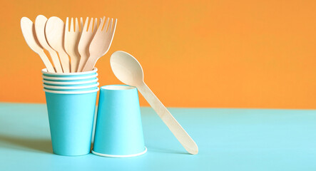 Wooden disposable forks and spoons in a blue paper cup, side view. Eco friendly disposable kitchen utensils on orange background, copy space. Ecological items concept