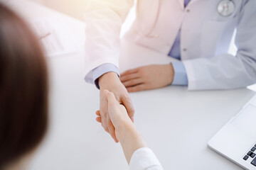 Doctor and patient shaking hands while sitting opposite of each other at the table in clinic, just hands close up. Medicine concept.