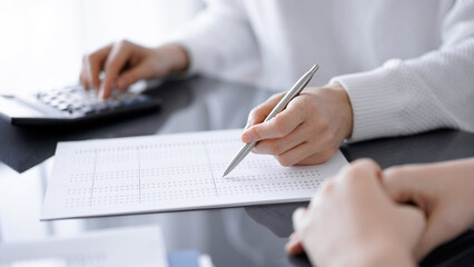 Woman accountant using a calculator and laptop computer while counting taxes for a client. Business audit concepts.