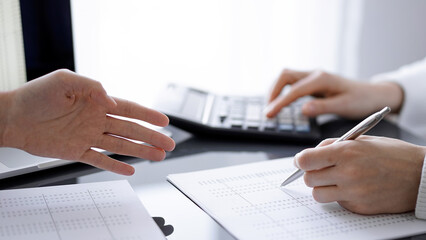 Woman accountant using a calculator and laptop computer while counting and discussing taxes with a client. Business audit concepts.