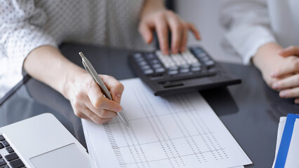 Woman accountant using a calculator and laptop computer while counting taxes for a client. Business audit concepts.