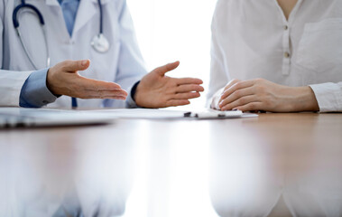 Doctor and patient discussing something while sitting near each other at the wooden desk in clinic. Medicine concept.