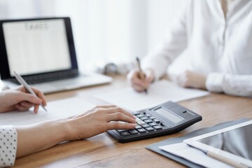 Two accountants using a laptop computer and calculator while counting taxes at wooden desk in office. Teamwork in business audit and finance.