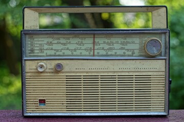 very retro old made in the ussr battery operated radio in a white plastic case stands on a brown wooden surface in the street during the day