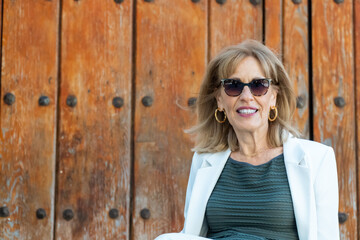 Portrait attractive middle aged woman wearing sunglasses smiles posing with old wooden door behind