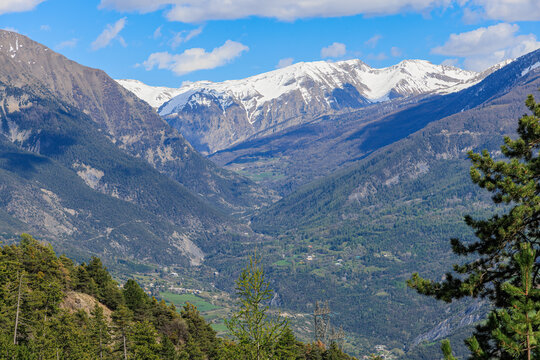 A scenic view of a mountain valley with a town surrounded by snowy mountain summit under a majestic blue sky