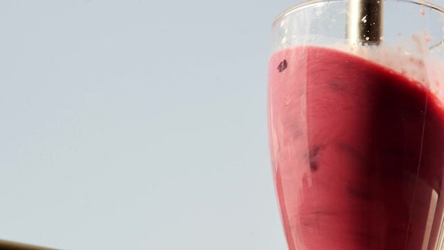 Super close-up of the process of making a milk-based fruit and berry smoothie using an immersion blender. Grinding cherries in a glass of milk using a blender. nutritious milky natural drink