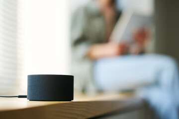 Close-up of smart speaker to listen to music or news with woman resting in background
