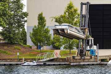 Pontoon boat removed from dry dock marina storage warehouse resting on fork lift ready for launch.