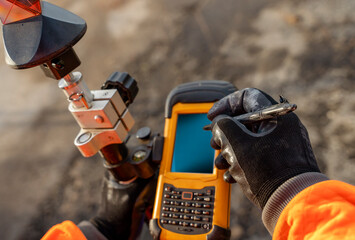 Site engineer operating his touch screen controller instrument during roadworks. Builder using touch screen controller to control total positioning station tachymeter on construction site