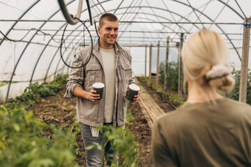 Thoughtful man bring two cups of coffee for him and his colleague in the greenhouse.