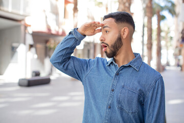 young handsome man looking bewildered and astonished, with hand over forehead looking far away,...