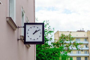 A square clock with hands on the building shows ten minutes past two - obrazy, fototapety, plakaty