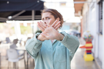 pretty young woman covering face with hand and putting other hand up front to stop camera, refusing...