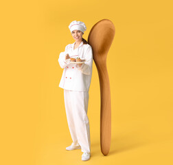 Female confectioner with tasty muffins and big wooden spoon on yellow background