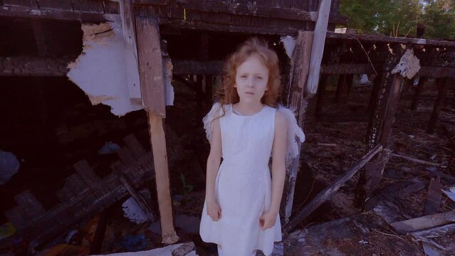 Sad child girl on the background of a burned-out house. Child angel near the destroyed house.