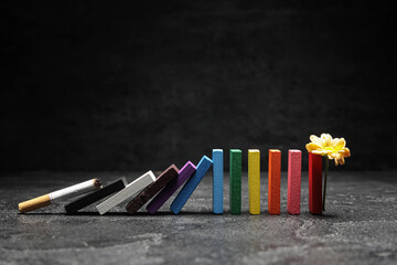 Obraz premium Row of colorful chalks, cigarette and flower on dark background. Stop smoking concept