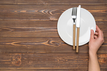 Female hand with empty plate and cutlery on brown wooden background
