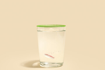 Glass of water with soluble tablet on beige background