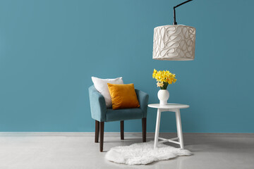 Cozy armchair with cushions and blooming narcissus flowers on coffee table near blue wall