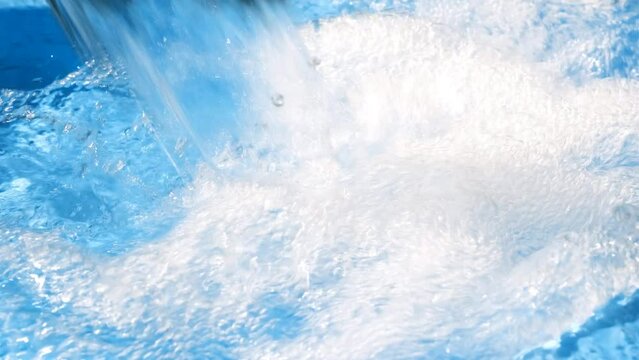 A jet of clear water with a blue tint flows into a blue container.