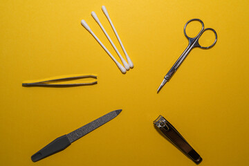 Fototapeta premium Cosmetic accessories with ear cleaners, scissors, nail clippers, nail file and tweezers on a yellow background