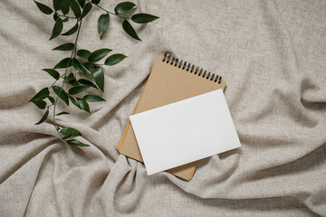 Blank invitation card, notebook and eucalyptus branches on grey crumpled tablecloth
