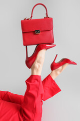 Female legs in red high heels with bag on grey background