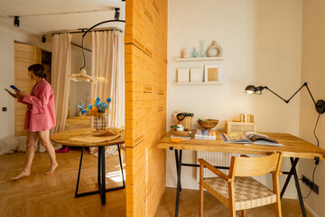 Interior view of workspace with a wooden table, dining space and woman walking in stylish studio apartement