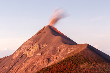 Volcan or volcano Fuego erupting with orange smoke column at sunrise, clear day near Antigua, Guatemala, Central America