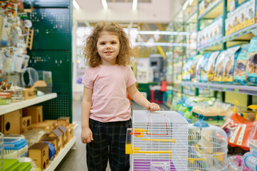 Portrait of little girl child standing nearby cage for rodent at pet shop