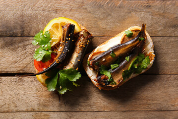 Tasty sandwiches with canned smoked sprats on wooden background - obrazy, fototapety, plakaty
