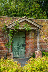 Fototapeta na wymiar Painted green door and wooden porch as entrance to walled garden made with brick