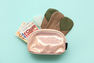 Lady's cosmetic bag with reusable menstrual pad, cup and money on turquoise background