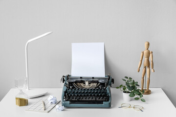 Vintage typewriter with wooden mannequin, lamp and eyeglasses on white table near wall