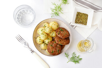 Bowl with cutlets, boiled baby potatoes and dill on white table in kitchen