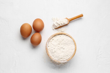 Fototapeta na wymiar Wooden bowl with wheat flour, scoop and eggs on white background