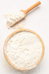 Wooden bowl with wheat flour and scoop on white background
