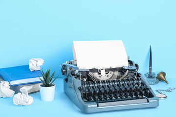Vintage typewriter with books, pocket watch and pen holder on blue background