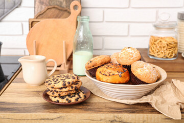 Bottle with milk, cookies and cupcakes on wooden table in kitchen