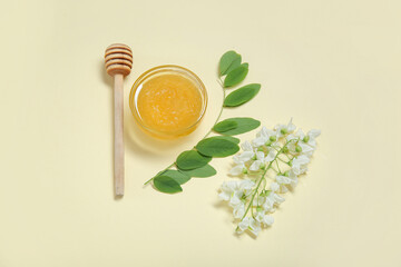 Bowl of honey with flowers of acacia and dipper on beige background