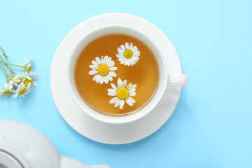 Teapot with cup of hot chamomile tea on blue background
