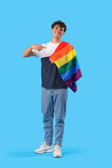 Fototapeta premium Young man pointing at LGBT flag on blue background