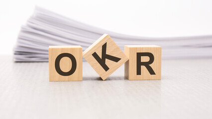 wooden block with text OKR - acronym - Objectives and Key Results. wooden blocks are on the paper white background, business concept. front view.
