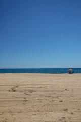View of a single sun umbrella and two sun beds at the dreamy and sandy beach of Mylopotas in Ios Greece