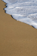 Close up of a beautiful sandy beach and white foamy waves in Ios Greece